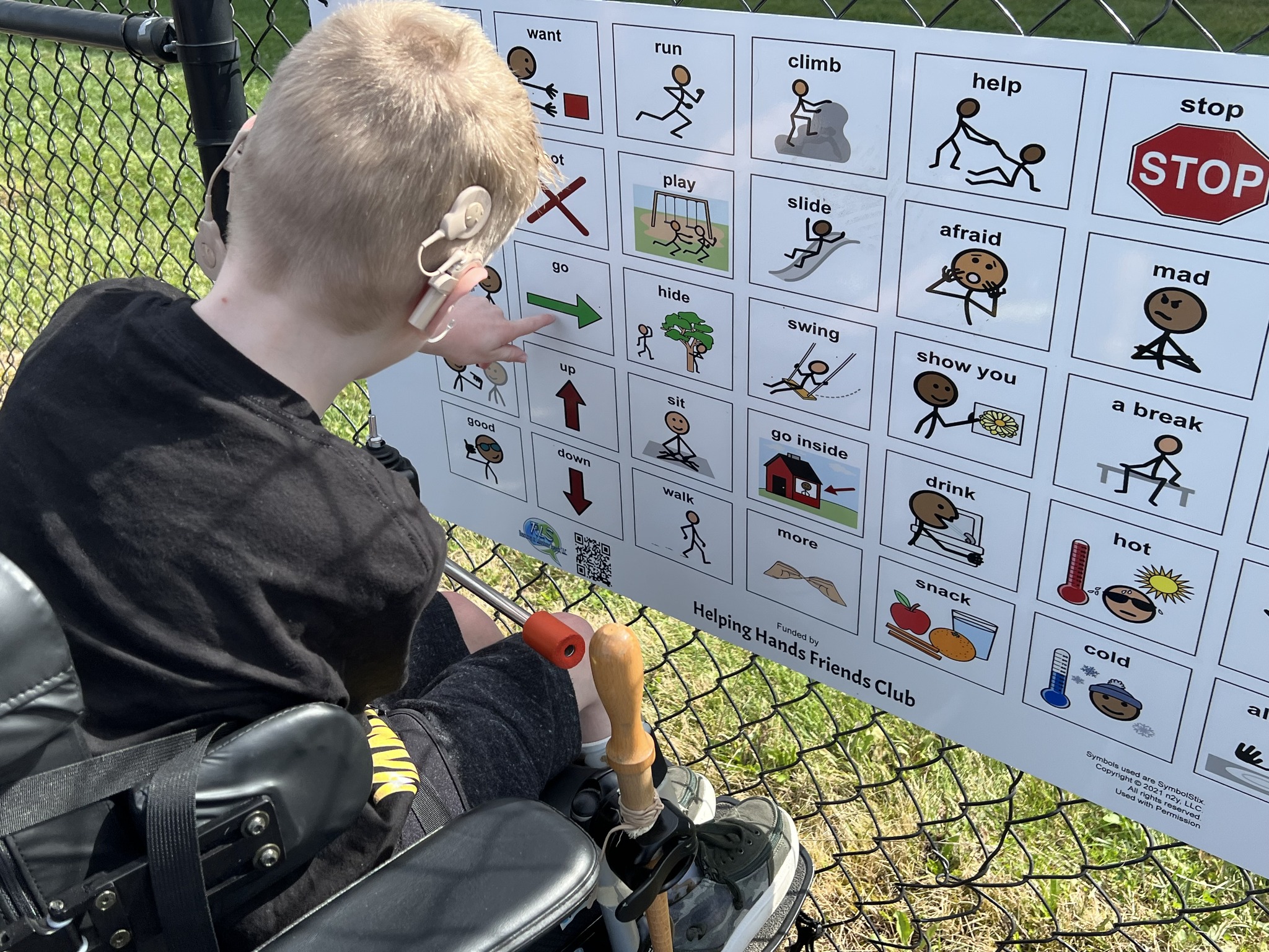 young man with cochlear implant pointing to a message on a playground communication board.