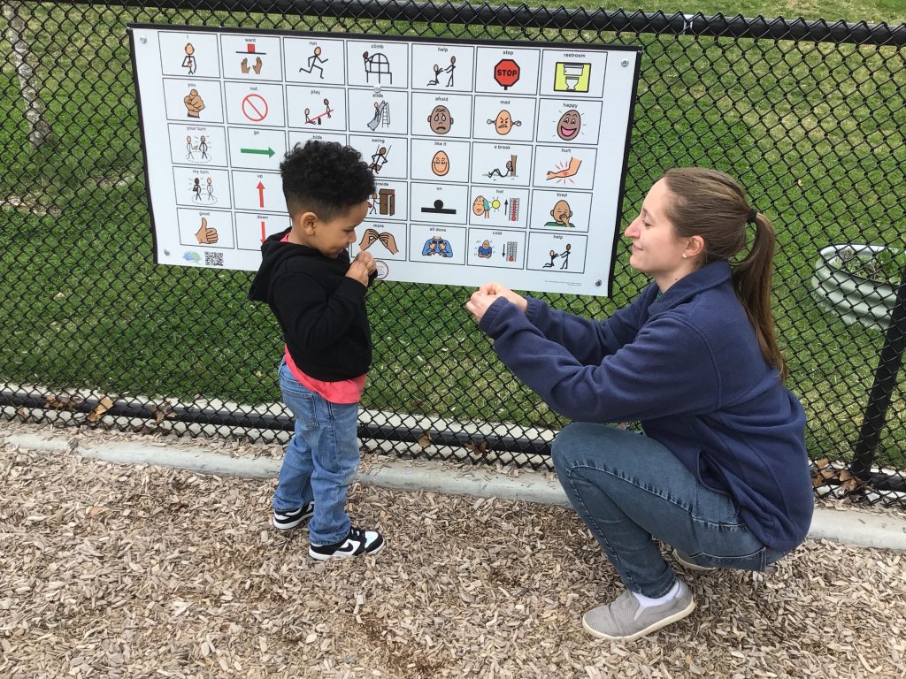 Communication board on a playground in use as a student to communicates 'more' with teacher